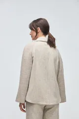 Sacón de diseño amplio con técnica patchwork, confeccionado con retazos de telas de diversas texturas en tonos beige y gris. Presenta mangas ranglan, cuello con solapas y cierre frontal con un único botón.