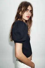 Jersey de punto negro con cuello redondo y mangas cortas abullonadas. Presenta una abertura frontal en forma de corazón.
