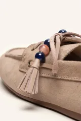Mocasín estilo náutico de gamuza marrón, con cordones de cuero, borla decorativa y cuentas de colores en el empeine.