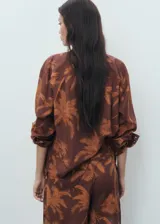 Camisa marrón de algodón con estampado de palmeras, cuello camisero, manga larga y cierre frontal de botones.
