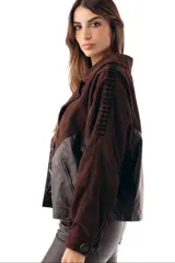 Campera bomber de cuero ovino negro combinada con gamuza chocolate, cuello solapa y cierre frontal de botones. Presenta mangas largas con detalles de costuras decorativas y bolsillos laterales ribeteados.