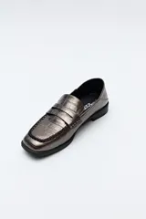 Mocasín de cuero sintético negro con punta cuadrada, detalle de costuras visibles en la capellada y taco bajo.