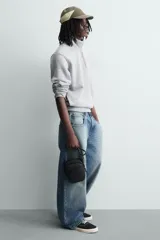 Bandolera vertical negra con acabado engomado, compartimento principal con cierre de cremallera y bolsillo interior plano. Bolsillo frontal con cierre de cremallera. Asa de hombro ajustable y extraíble.