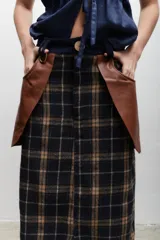 Falda larga de lana con estampado tweed a cuadros en tonos marrón y negro. Presenta detalles de cuero marrón en los bolsillos laterales y botón de guampa en la cintura.