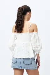 Top blanco con hombros descubiertos, bordado con detalles de puntilla y frunces en el frente. Tiene mangas abullonadas y breteles finos.