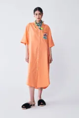 Vestido camisero color naranja de corte amplio, con largo irregular, cuello camisero, escote en V y tajo en los laterales.