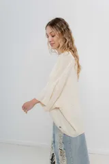 Sweater oversize de tejido liviano color blanco roto, con textura semi traslúcida, escote redondo y mangas amplias estilo murciélago.