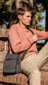 Morral bandolera de tela canvas color gris oscuro con detalles en negro. Tiene tapa con cierre, bolsillo frontal con cierre bajo la tapa, bolsillo trasero con cierre y correa larga regulable.