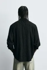 Camisa de hombre de corte relaxed fit, color negro, con textura de cuadros en relieve. Presenta cuello solapa, manga larga con puño abotonado y cierre frontal de botonadura.