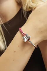 Pulsera semirígida compuesta por una estructura de metal bañada en plata de ley y una sección de cuero rosa, con un dije central en forma de mariposa de metal plateado.