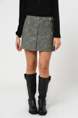 Minifalda gris con textura símil cuero, corte irregular con sobrefalda y cierre frontal con broches metálicos.
