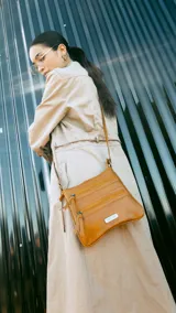 Bandolera color marrón con apertura superior de cierre metálico y dos bolsillos frontales con cierre. Incluye correa larga regulable y placa metálica con el logo de la marca.