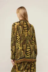 Camisa de viscosa estampada con diseño de plumas en tonos amarillo y negro. Tiene cuello clásico, mangas largas con puños abotonados, cierre frontal con botones y corte tradicional.