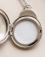 Collar de cadena fina con dije de acero en forma de mariquita que funciona como camafeo, permitiendo abrirlo para guardar una fotografía.