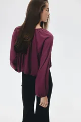 Blusa color vino tinto, con cuello redondo y escote en V con cordones para atar. Presenta mangas globo largas y un bajo fruncido con efecto burbuja.