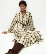 Vestido largo de corte midi, confeccionado en tejido de viscosa con estampado de cuadros. Presenta cuello camisero, cierre frontal abotonado, mangas largas abullonadas y falda con volados. Incluye un cinturón fino para ajustar a la cintura.