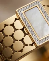 Esclava rígida de acero con baño de oro, con diseño de malla hexagonal calada. Presenta un aplique central rectangular con incrustaciones de circonias y centro de nácar.