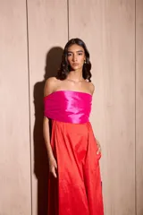 Vestido largo strapless con corpiño fruncido en color fucsia brillante y falda amplia en color rojo vibrante. La prenda tiene bolsillos laterales.