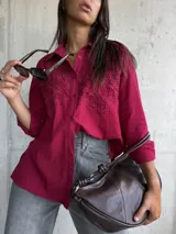 Camisa de color bordó con cuello clásico y cierre frontal de botones. Presenta un diseño distintivo con paneles de encaje bordado en la parte superior delantera, mangas largas con puños y un corte recto.