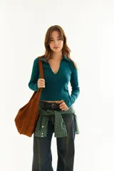 Top de manga larga color verde petróleo, con cuello polo y escote en V pronunciado. Presenta recortes diagonales en el frente y un pequeño bordado en el puño.