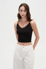 Musculosa crop de morley negro con tirantes finos, escote en V decorado con detalles de encaje y un pequeño lazo en el centro.