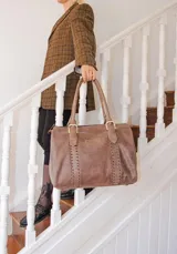 Bolso de mano tipo shopper marca Amadea, confeccionado en cuero con acabado desgastado. Presenta detalles de costuras decorativas verticales, correas con hebillas metálicas doradas y logo grabado al frente.