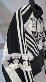 Campera corta con cierre frontal, confeccionada en una combinación de tela y apliques de cuerina, con diseño bicolor en blanco y negro, cuello alto y estampas de estilo motociclista.