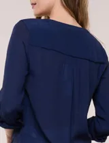Blusa de calce relajado color salmón, confeccionada en tela liviana con textura sutil. Presenta escote en V con abotonadura frontal, bolsillo parche en el pecho, mangas largas regulables con presilla y ruedo con opción de anudar en el frente.