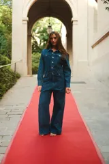 Mono de denim azul con cierre frontal de botones metálicos, cuello camisero, mangas largas y bolsillos delanteros.