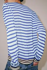 Jersey de punto fino con diseño de rayas horizontales en tonos azul claro y azul oscuro. Presenta cuello redondo, manga larga y detalles de rayas en contraste en los puños y el ruedo.