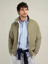 Campera Harrington color beige, con cuello alto abotonado, cierre frontal completo y bolsillos laterales con solapa y botones a presión. Puños y cintura elastizados de rib.
