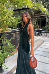 Vestido largo verde oscuro de terciopelo y satén, con escote halter pronunciado y diseño ajustado en el torso con caída fluida en la falda.