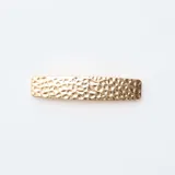 Pack de dos pinzas para el cabello en tono dorado, una con diseño de líneas paralelas y otra con textura martillada.