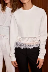 Sudadera crop de cuello redondo y manga larga con puños elásticos. Presenta un diseño de doble capa con un top interior satinado y un bajo decorado con encaje a tono.