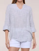 Blusa de silueta relajada con textura tramada, color azul con rayas verticales en tonos rosados, celestes y amarillos. Cuenta con cuello mao abierto en V y mangas tres cuartos amplias con pequeña abertura lateral en el puño.