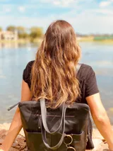 Mochila negra de cuero convertible en bolso de mano o bandolera. Tiene compartimento para laptop, bolsillos exteriores y correas ajustables y extraíbles.