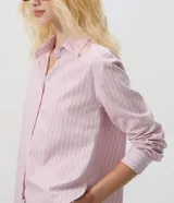 Camisa oversized de popelina de algodón, con diseño a rayas en tonos rosados y azules, cuello clásico, mangas largas con puños abotonados y cierre frontal de botones.