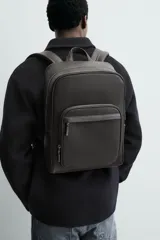 Mochila de diseño minimalista con acabado grabado, compartimento principal con cierre, espacio interior para dispositivos electrónicos de hasta 13 pulgadas, bolsillos frontales con cierre, parte posterior acolchada con banda de sujeción para equipaje, asa de mano y correas de hombro ajustables y acolchadas.