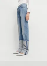 Pantalón de jean de corte recto y tiro medio, confeccionado en algodón. Presenta un diseño distintivo con el bajo vuelto en un tono de denim más claro y una costura lateral vertical en contraste.