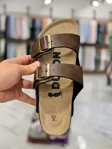 Sandalias de dos tiras negras con hebillas metálicas ajustables, plantilla anatómica y suela plana.