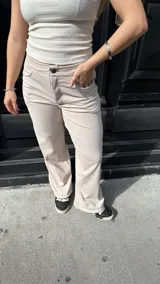 Pantalón de corte recto y tiro medio, confeccionado en tejido jersey rib color beige. Presenta bolsillos traseros y etiqueta de marca en la cintura posterior.