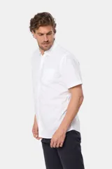 Camisa lisa de manga corta color crema, confeccionada en 100% algodón, con cuello abotonado y un bolsillo en el pecho.