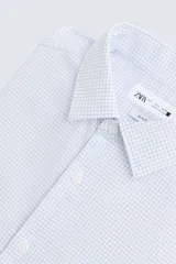 Camisa de manga larga para hombre, corte slim fit, con cuello italiano y cierre frontal de botonadura. Presenta un microestampado de cuadros pequeños en tonos blanco y celeste.