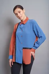 Camisa de poliéster color block azul y naranja con detalles en negro, de corte asimétrico y mangas largas con presilla para sujetar.
