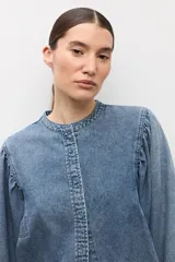 Camisa de jean de corte clásico con cuello mao, cierre frontal con botones y mangas largas abullonadas con puños elásticos.