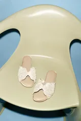 Sandalia plana tipo pala de color beige, con tira ancha decorada con perlas y abalorios brillantes dispuestos en patrón radial, punta redonda y suela plana.