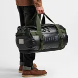 Bolso de viaje tipo duffle negro con detalles en verde, marca Roark, modelo Pony Keg 60L. Tiene doble asa de mano con agarre acolchado, correa de hombro ajustable y extraíble, bolsillo frontal con cierre y logo estampado. Se puede usar como bolso de mano o como mochila.