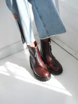 Botas de cuero color marrón con suela track negra y cierre frontal con cremallera roja.