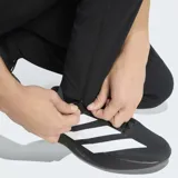 Pantalón deportivo Adidas del Real Madrid, modelo Tiro Travel, color negro. Presenta un diseño técnico con corte clásico, cintura elástica, costuras ergonómicas para mayor movilidad y bolsillos laterales. Incluye el escudo del club y el logo de la marca en tono sobre tono.