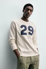 Camiseta relaxed fit de algodón con estructura waffle, color beige. Presenta un parche con el número "29" en azul marino en el pecho. Tiene cuello redondo y manga larga con acabados en rib.
